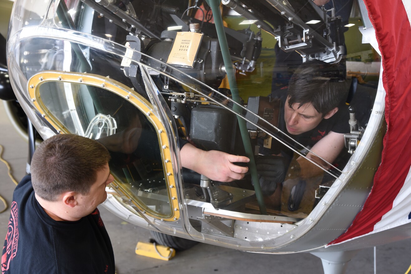 Museum restoration specialists Nick Almeter and Casey Simmons install a bomb sight in the Boeing B-17F Memphis Belle.